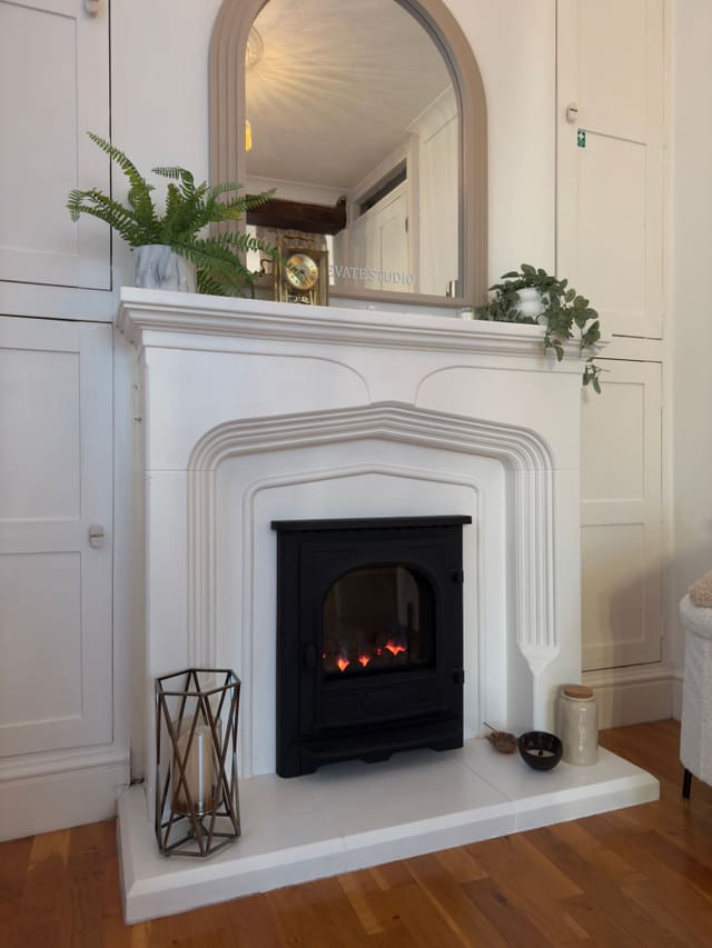 The white stone fireplace beneath an arched mirror, with a fern and a lantern on the hearth