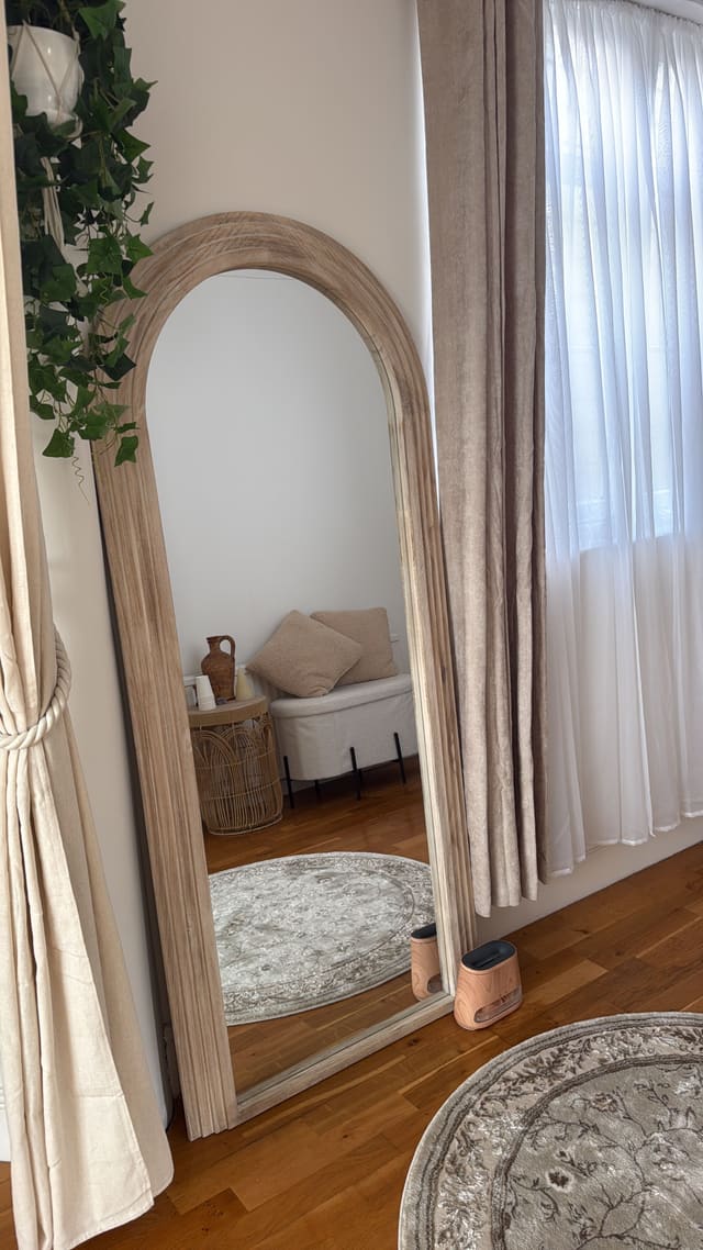 A tall arched floor mirror with warm lamps glowing on the wooden floor
