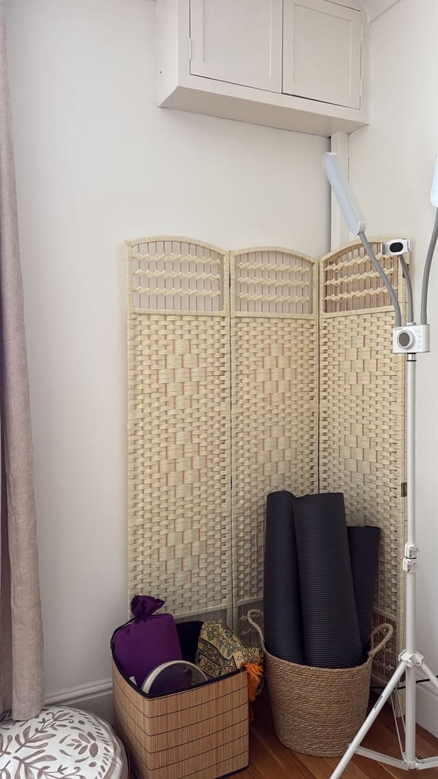 Yoga mats in a basket beside a woven screen and a light stand