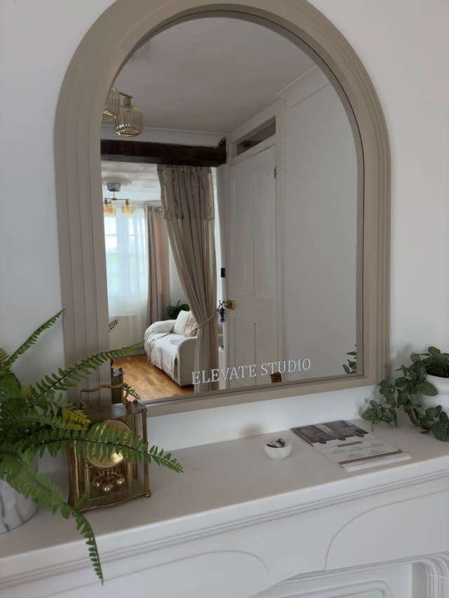 An arched mirror etched with ‘Elevate Studio’ above the mantel, with ferns and a brass clock