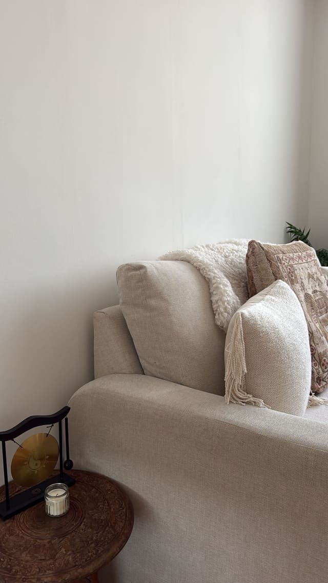 A sofa corner with a small brass gong and a candle on a carved side table