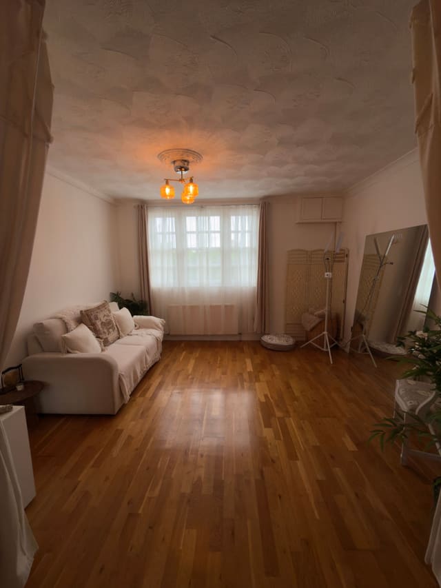 The open studio room with a cream sofa, wooden floors and windows dressed in sheer curtains