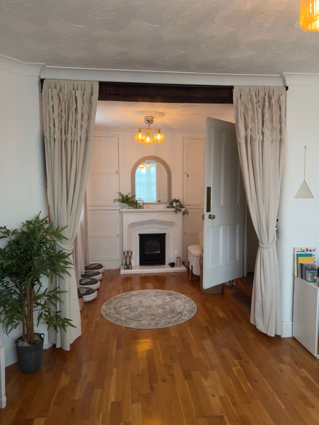 A view through draped linen curtains to the fireplace, with floor cushions and a round rug