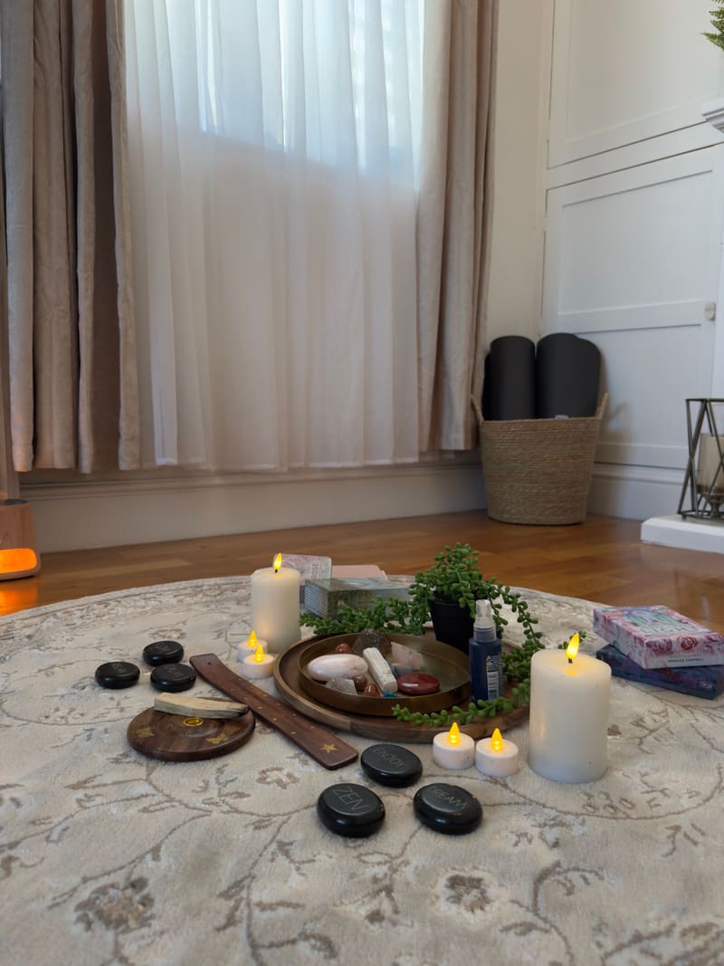 Candles, crystals, smooth stones and a trailing plant arranged on a round rug, ready for a wellbeing session