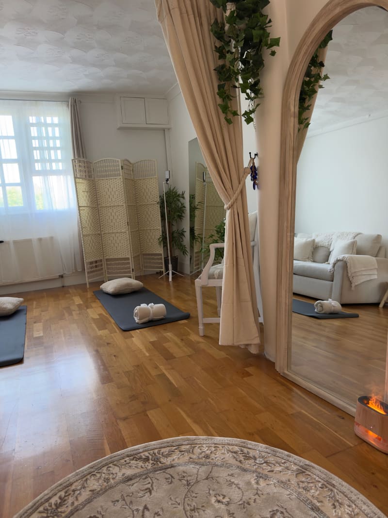 Yoga mats and cushions laid out across the studio’s wooden floor, seen past a tall arched mirror