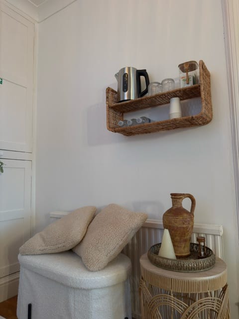 A rattan shelf with a kettle, glasses and herbal teas above two soft bouclé cushions